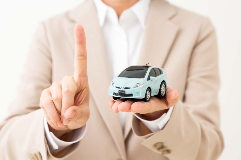 手のひらに乗せた車のミニチュアと指を立てるビジネスパーソン