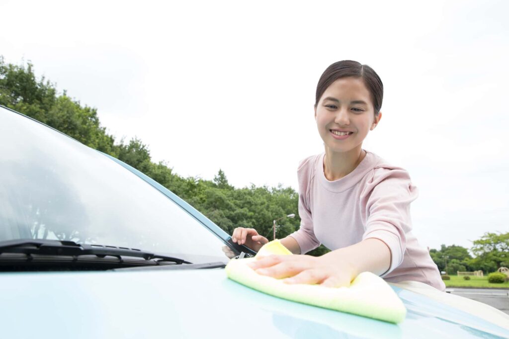 青い車のボンネットを拭き上げる笑顔の女性