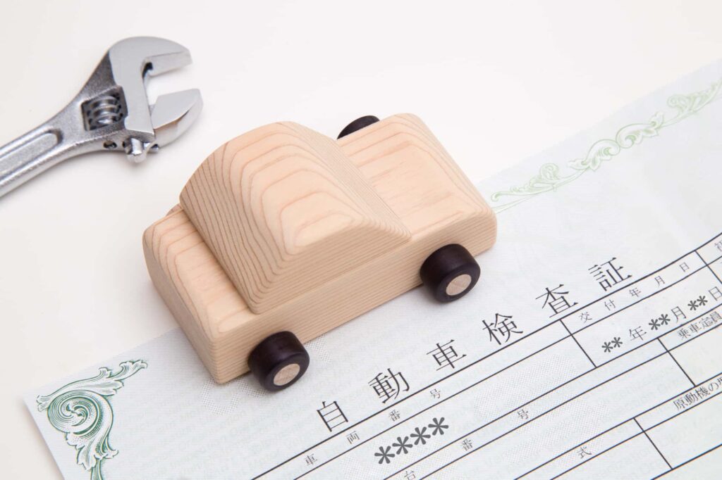 車検証と木製のミニカー、スパナのイメージ