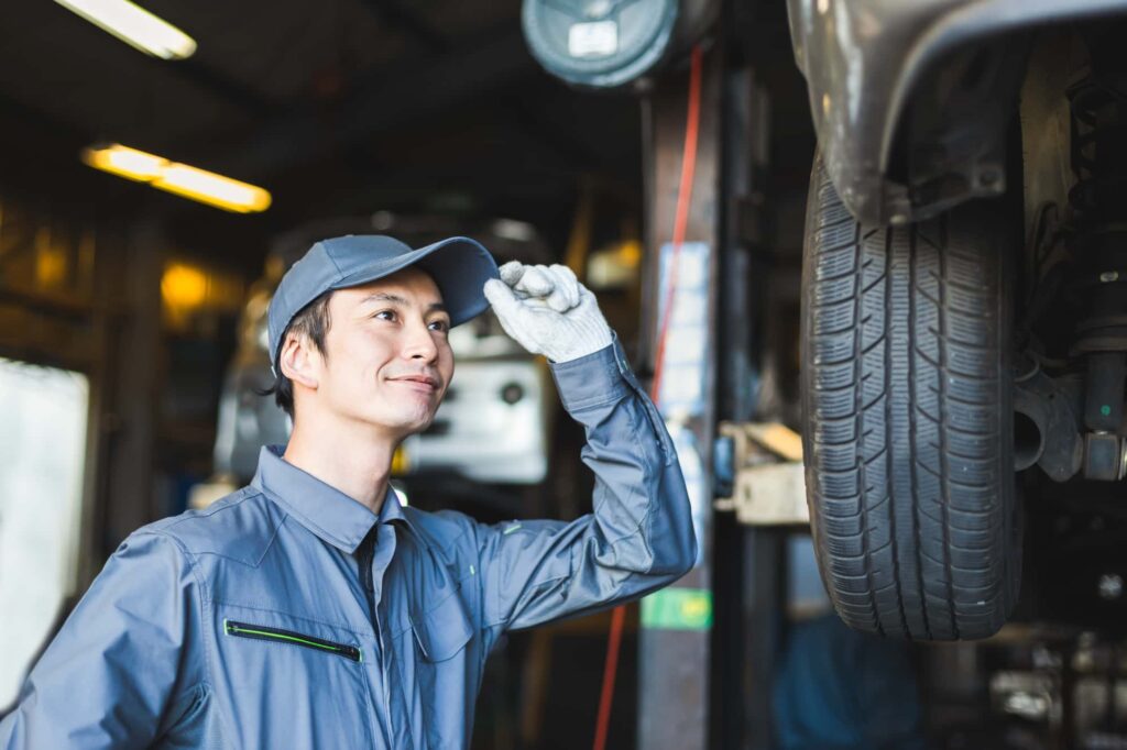 整備工場で作業中の整備士が笑顔で帽子に手を添えている様子