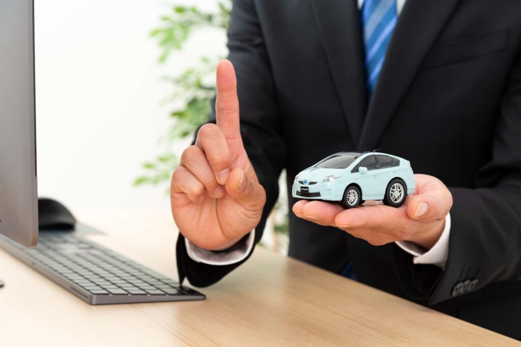 手のひらに車のおもちゃと人差し指を立てる男性