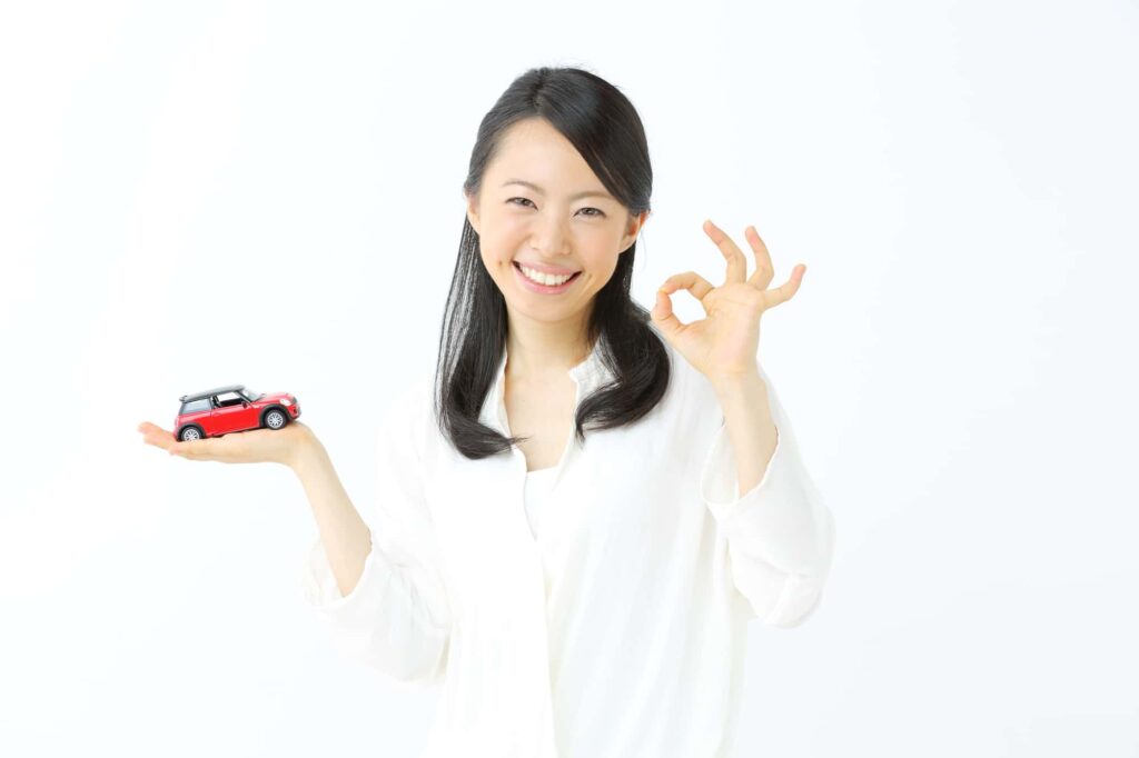 ミニカーを持ち笑顔でOKポーズをする女性