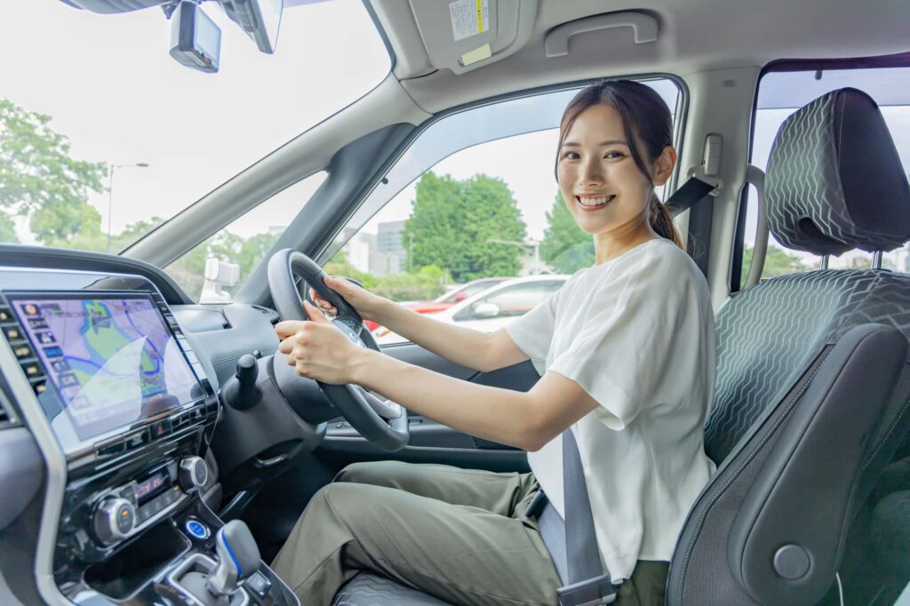 ハンドルを握りながらこちらを絵がをで見ている女性