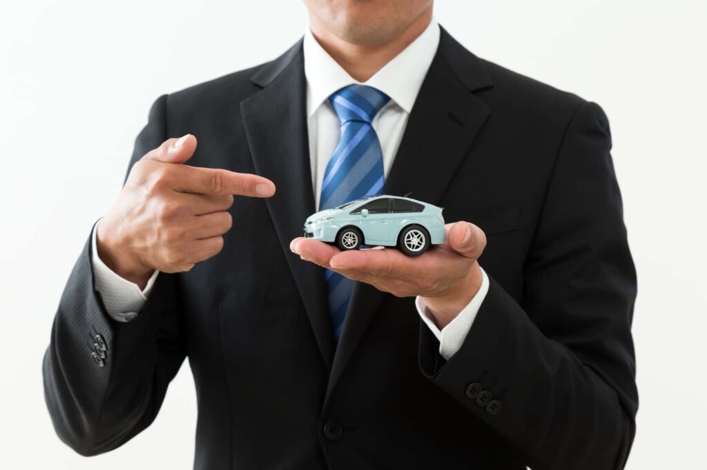 スーツの男性が手のひらに乗せたミニカーを指差している様子