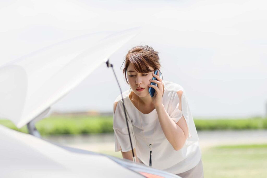 ボンネットを開けて電話する女性