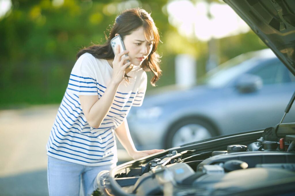 故障した車を見て電話する女性
