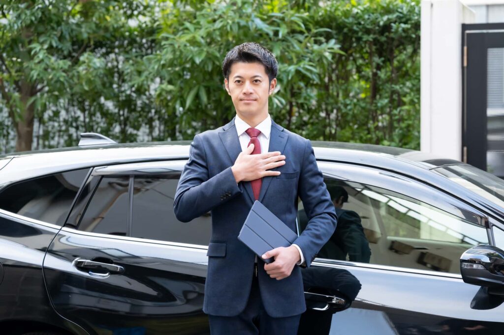 車の前で胸に手を当てるビジネスマン