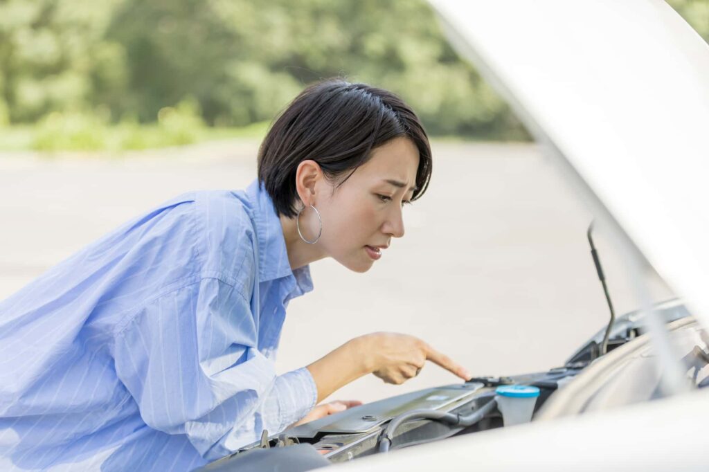 車のボンネットを開けてエンジンルームを覗き込み、何かを指差す女性