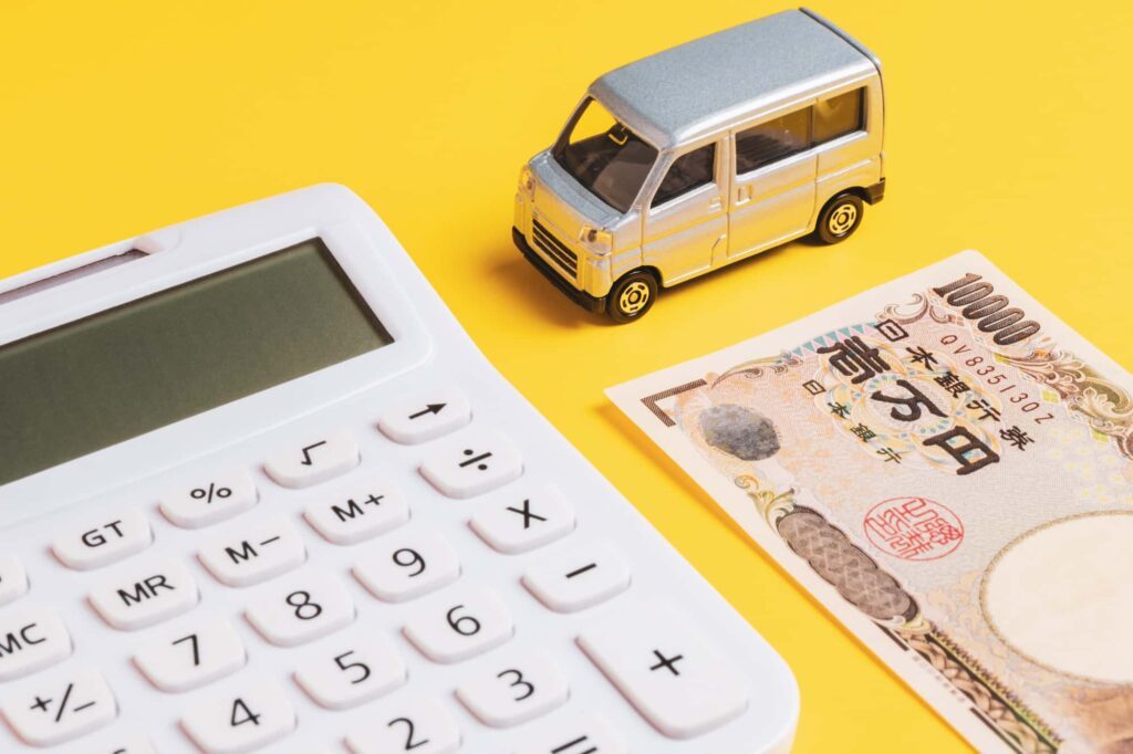 ミニカー、電卓、一万円札が黄色い背景に置かれている