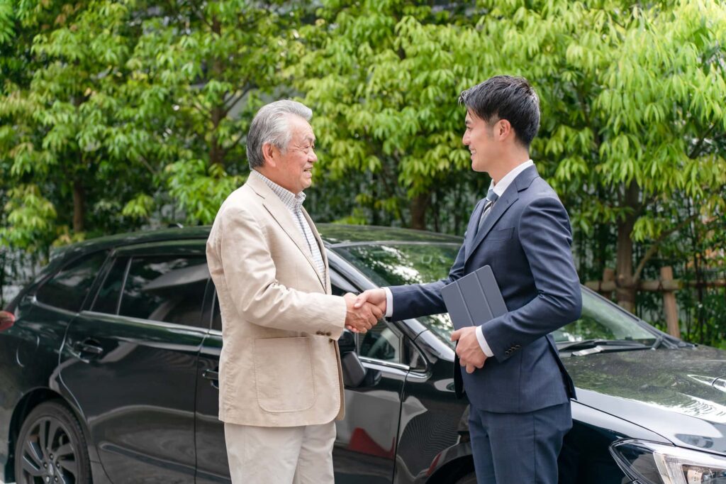 車の前で握手するビジネスマンと高齢男性