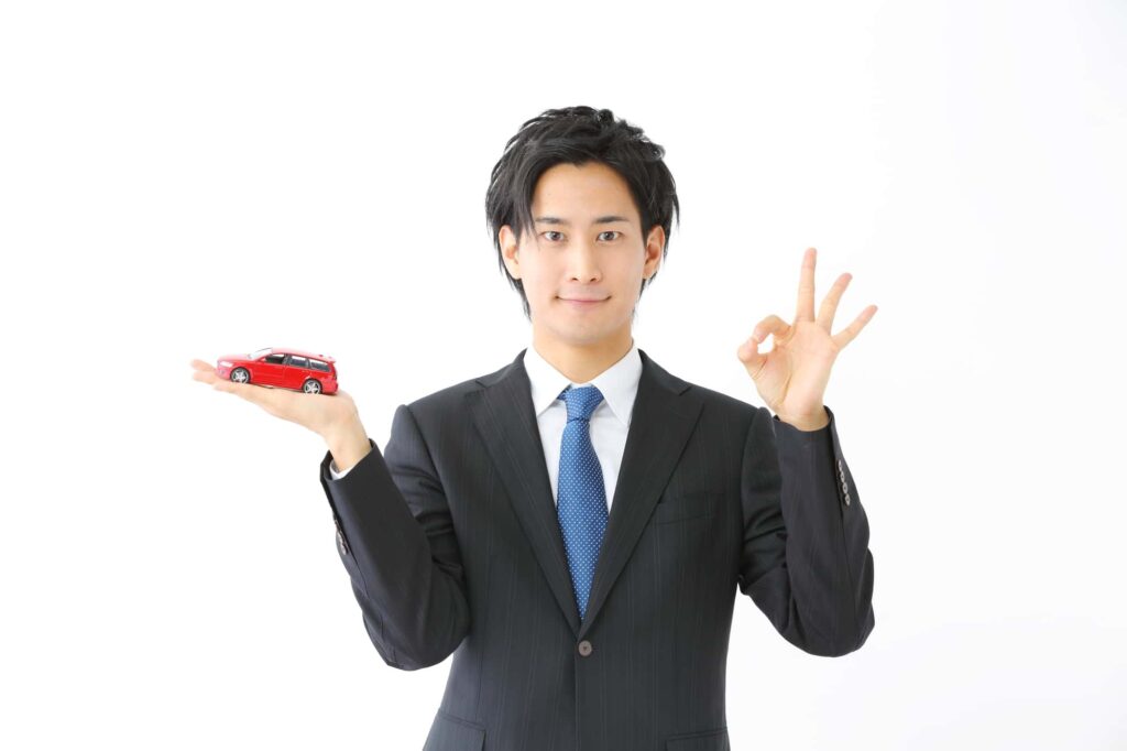 ミニカーを手にOKサインをするビジネスマン