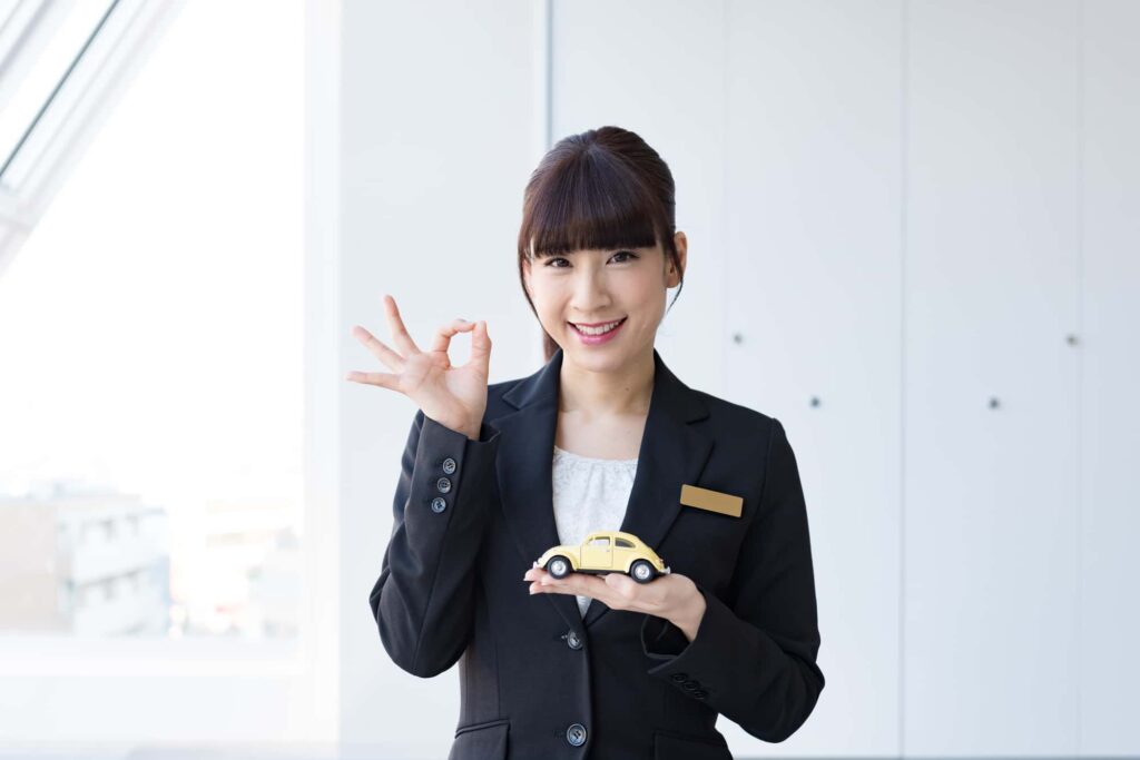 ミニカーを持ってOKサインをする女性スタッフ
