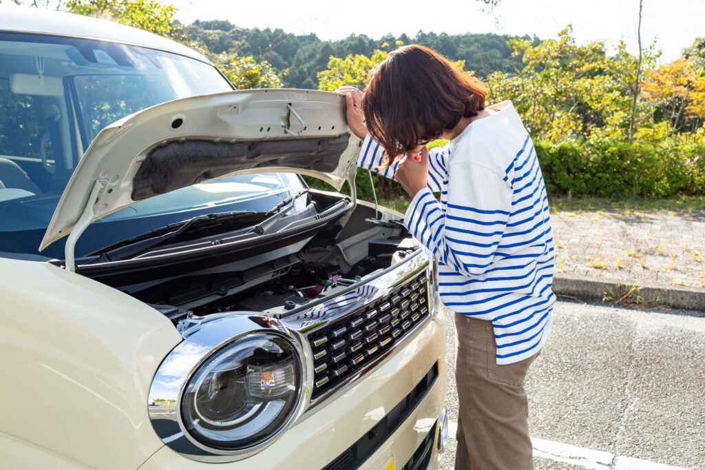車のエンジンルームを覗き込む女性