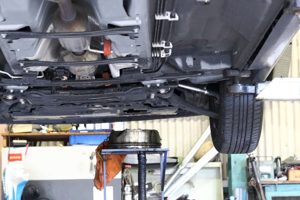 リフトアップされた車の底部、エンジンオイル交換のために用意されたオイル受け皿