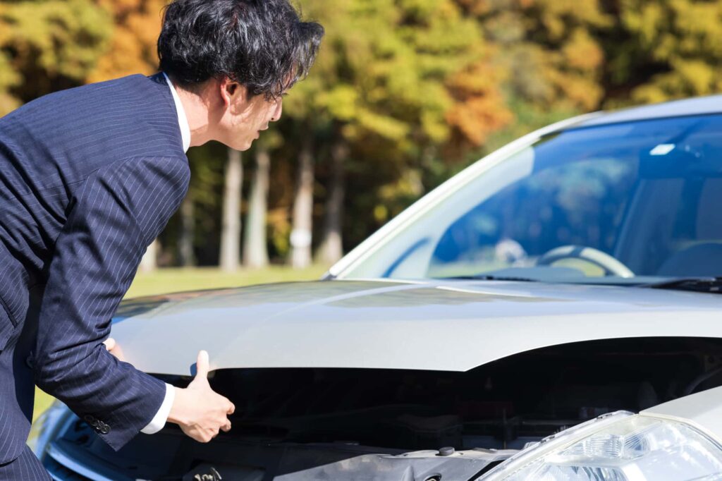 車のボンネットを開けてエンジンルームを覗き込むスーツ姿の男性