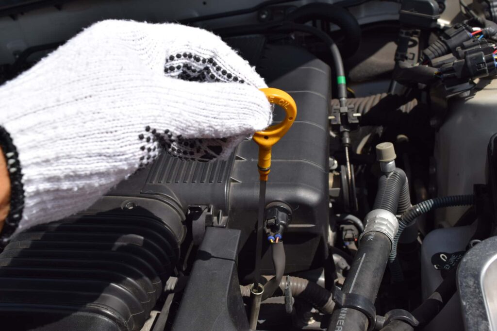 白手袋をはめた手が、車のエンジンオイルレベルゲージを引き抜く瞬間